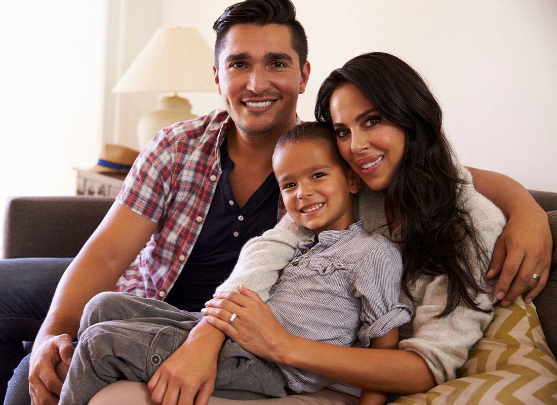 Insurance Solutions - Family Portrait of a Young Father, Mother, and Child Sitting on the Family Room Sofa