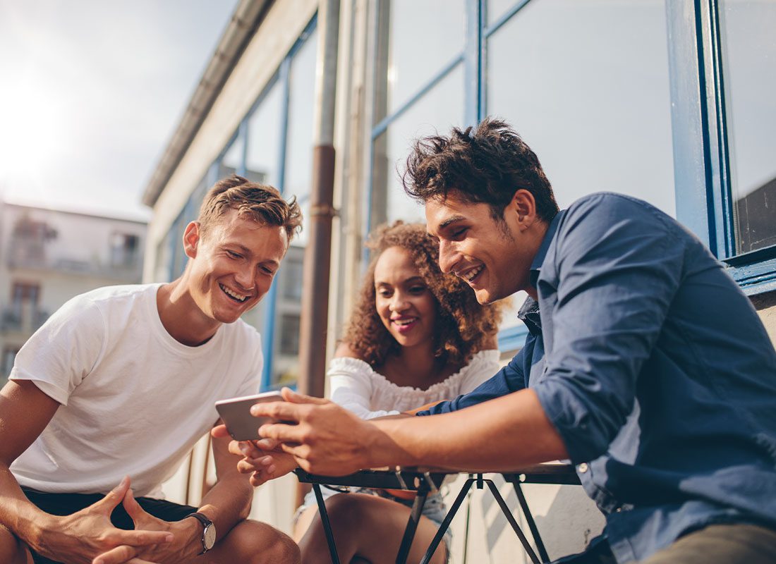 Video Library - Friends Gathering Around a Phone to Watch a Video Outdoors Against a Modern Office Building